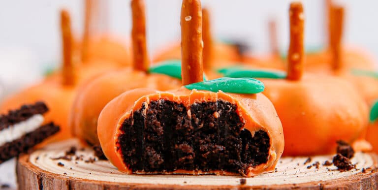 Close-up of orange candy chocolate pumpkins with pretzel stems and green leaves with one missing a bite.