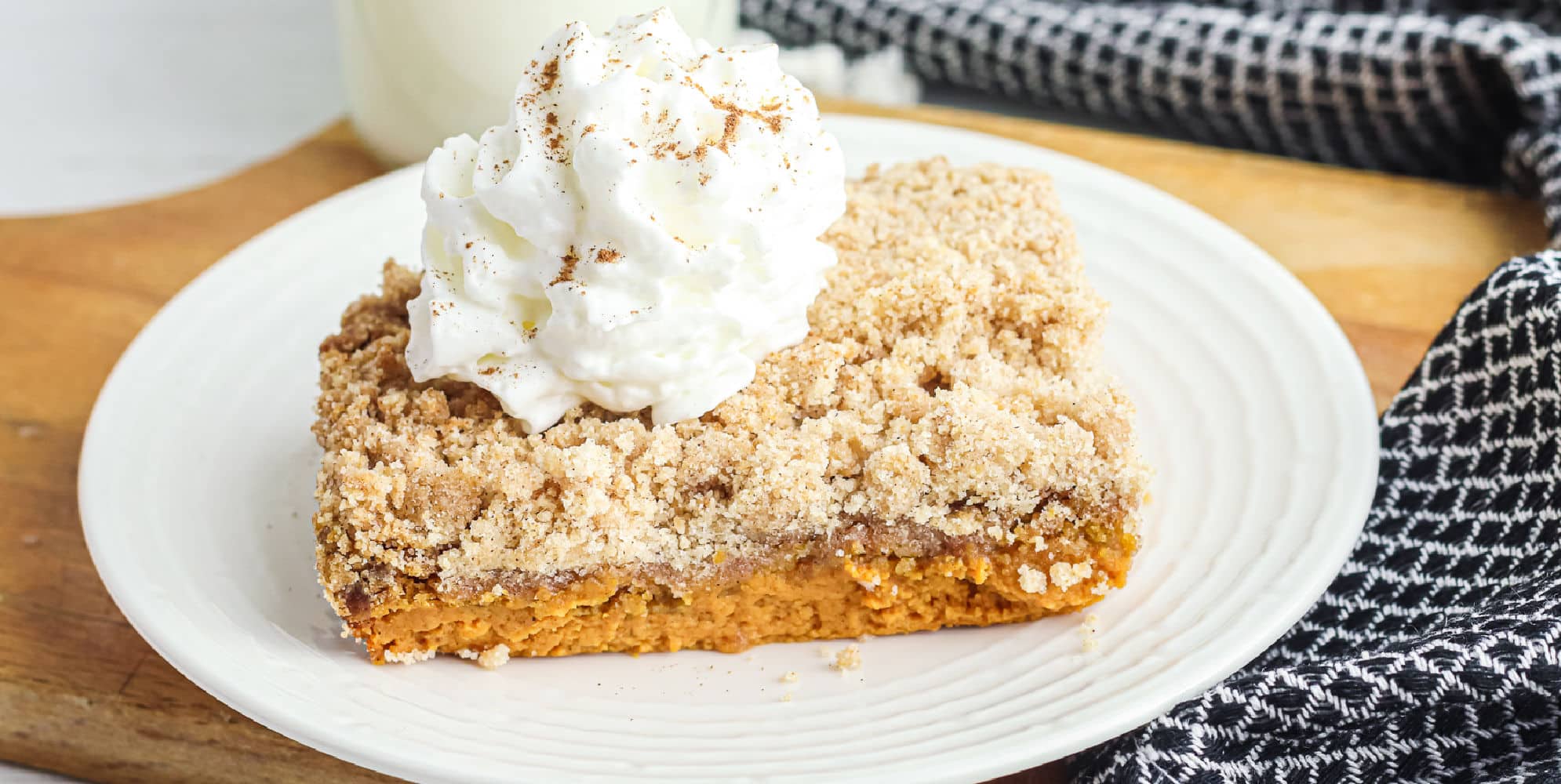 A slice of pumpkin dump cake with a crumb topping and whipped cream on a plate.