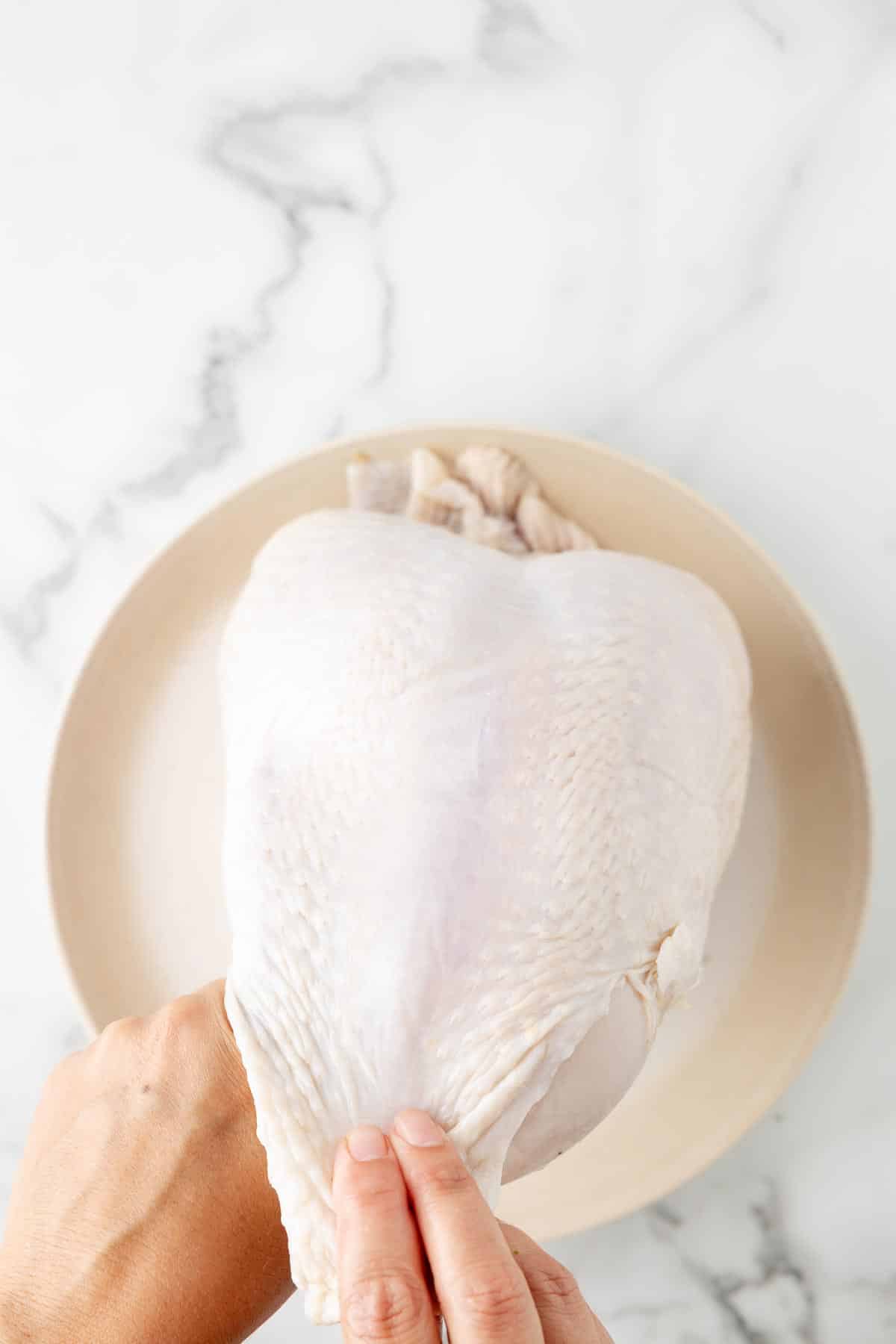 A person's hands gently separating the skin from a bone in turkey breast on a plate to season under the skin.