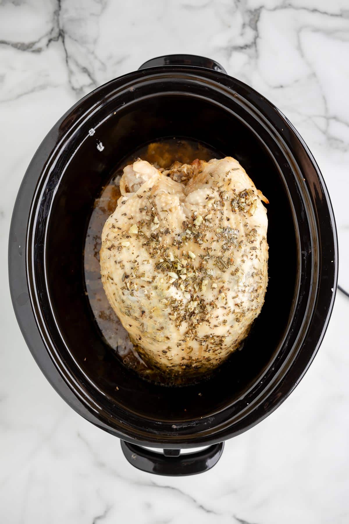 A seasoned whole chicken cooked in a slow cooker on a marble countertop.