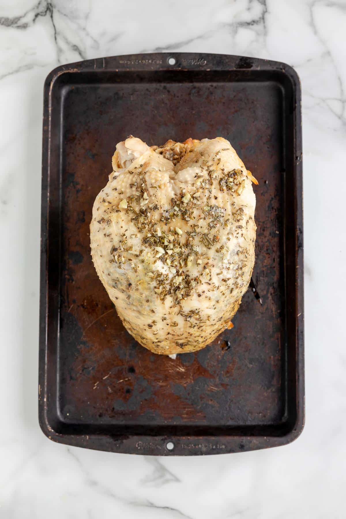 Cooked, herb seasoned turkey breast on a dark baking tray on a counter.