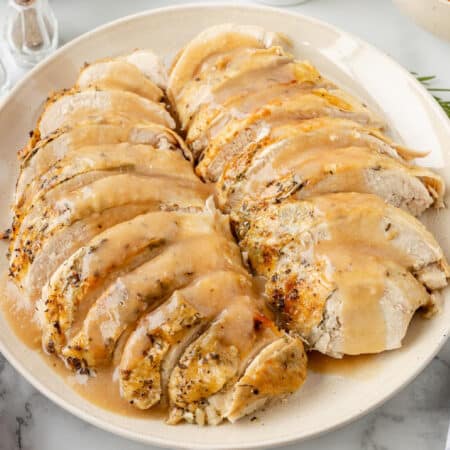 Sliced roasted turkey breast on a plate, drizzled with gravy.