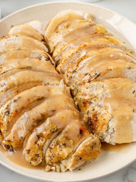 Sliced roasted turkey breast on a plate, drizzled with gravy.