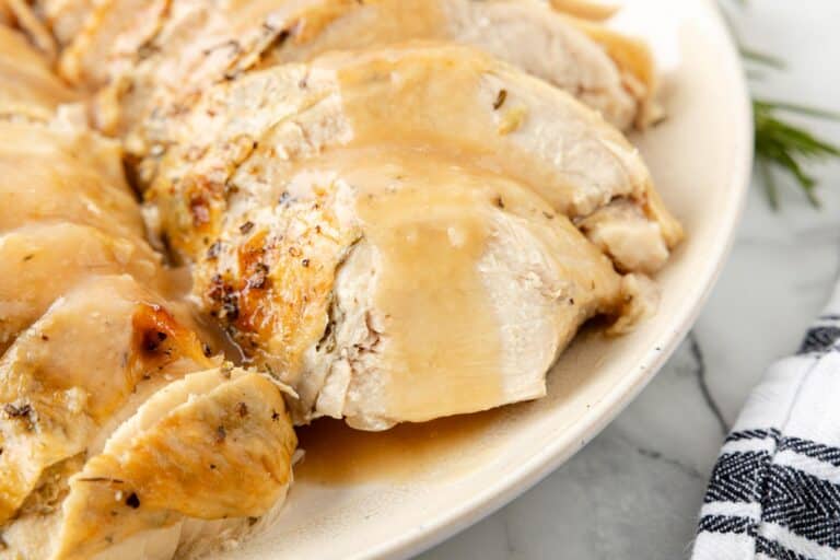 Sliced roasted turkey breast with gravy on a white plate.