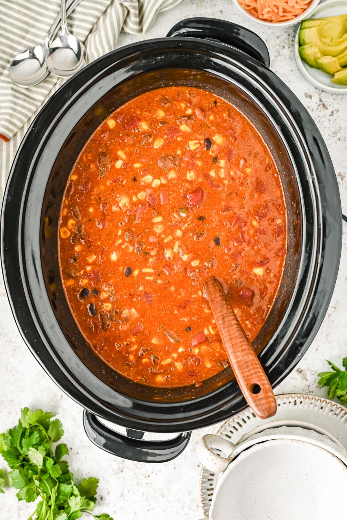 A slow cooker filled with 7 can soup while a wooden spoon stirs.