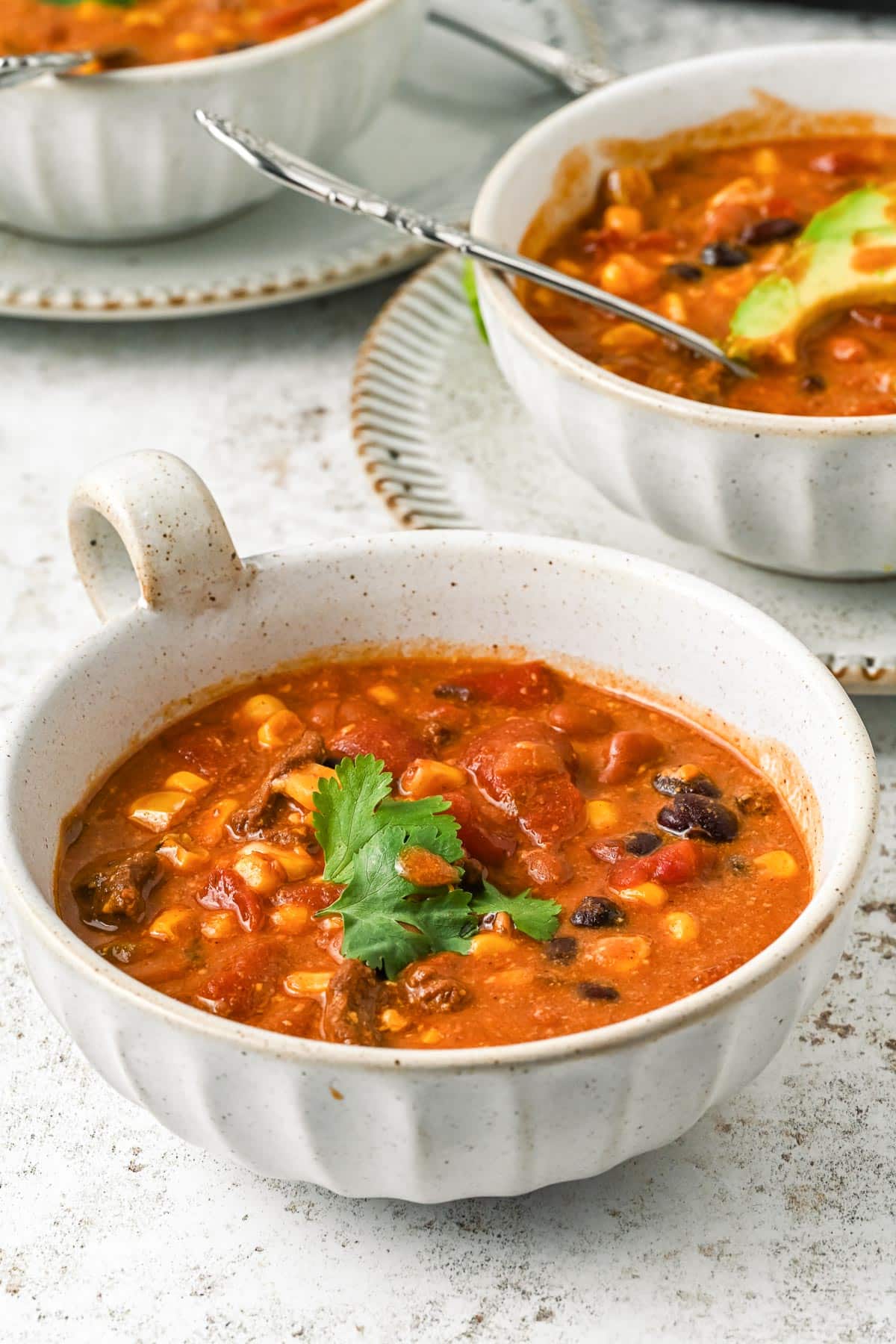 A bowl of hearty 7 can soup with beans, corn, tomatoes, with more bowls in the background.