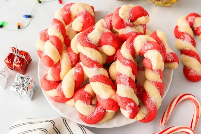 A plate of red and white twisted candy cane-shaped cookies on a table next to a few Christmas decorations.