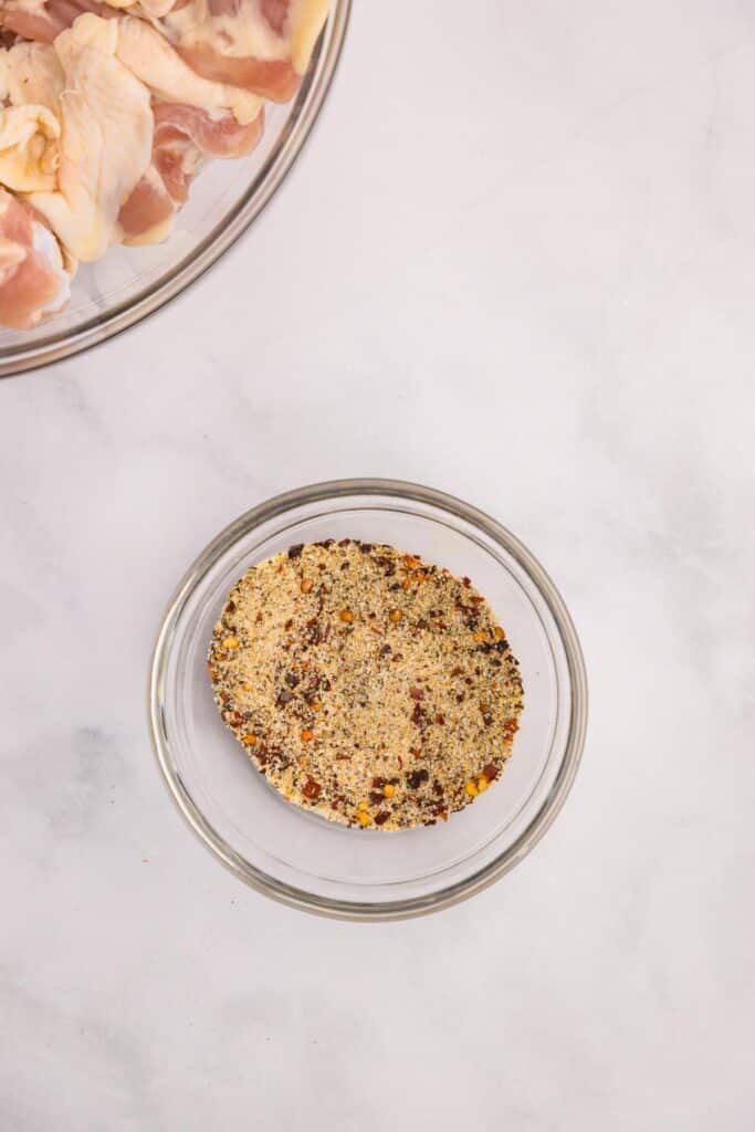 A bowl of spices mixed together next to a bowl of raw chicken thighs on a counter for chicken thighs and rice.