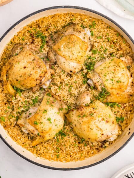 A square view of a pot with cooked chicken thighs and rice.