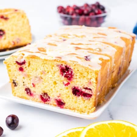 Wide view of a loaf of cranberry orange bread topped with a drizzle of frosting.