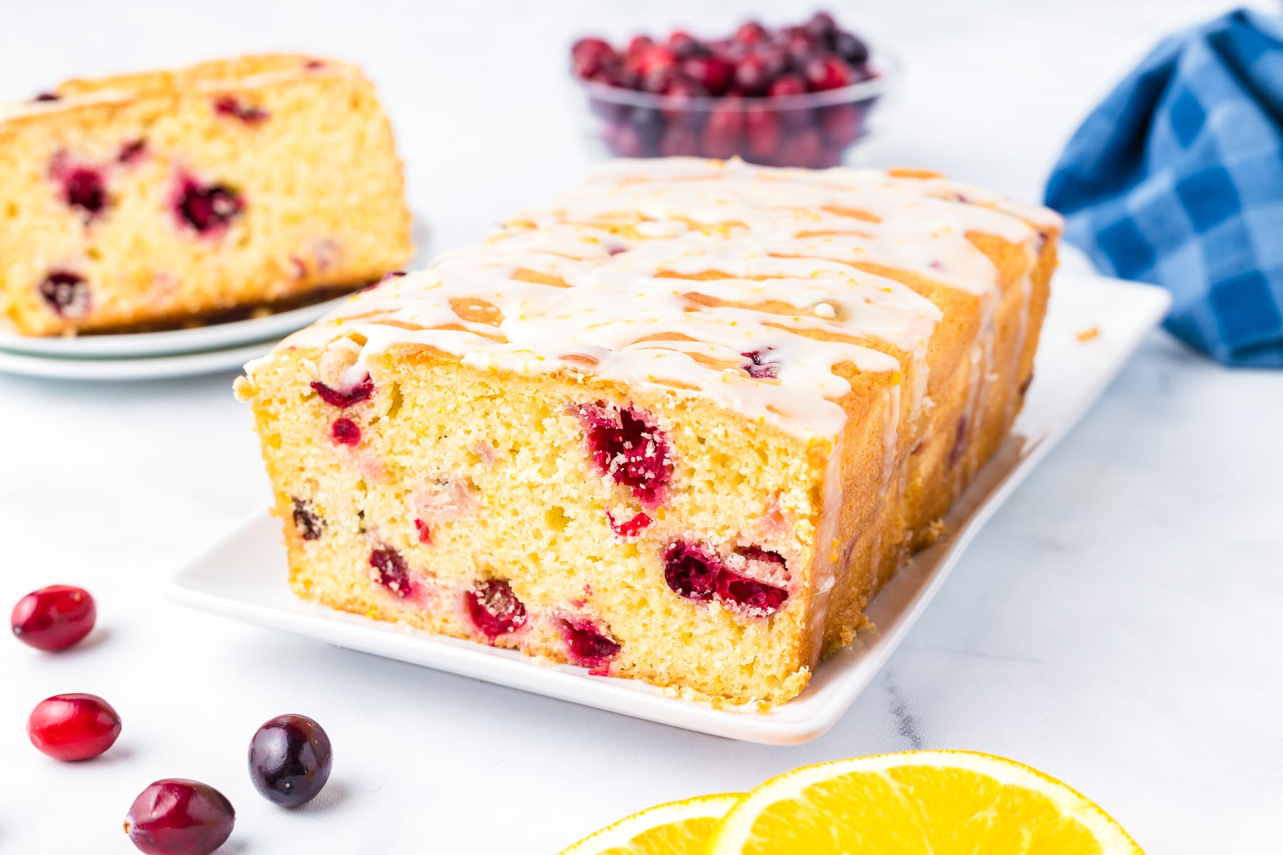 Wide view of a loaf of cranberry orange bread topped with a drizzle of frosting.