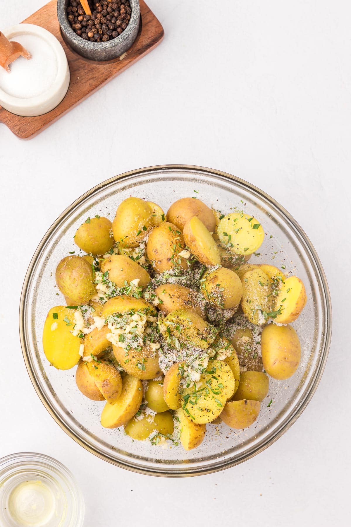 A bowl of halved baby potatoes being mixed with seasoning and oil to roast.