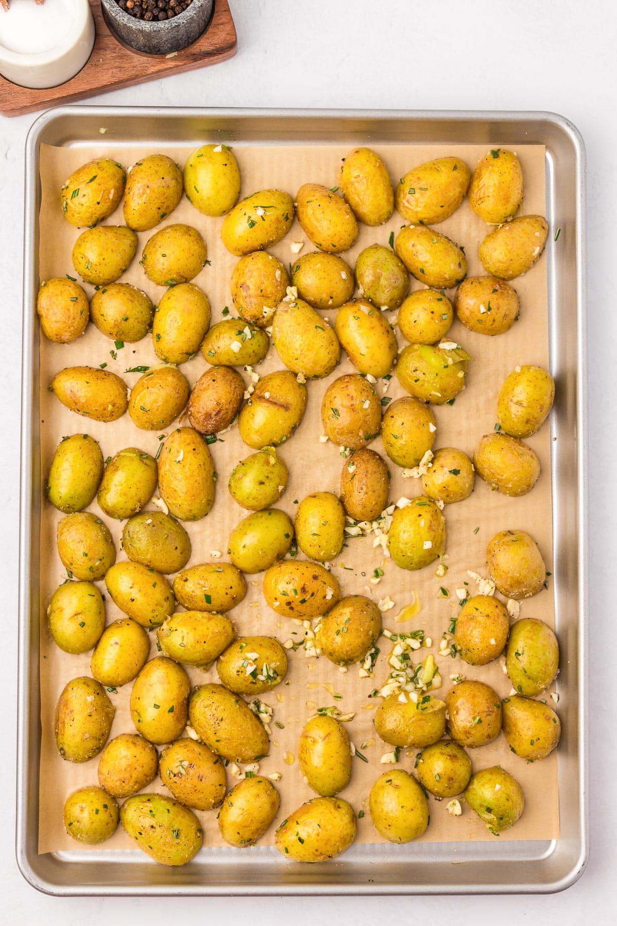 A baking sheet with roasted baby potatoes seasoned with herbs and garlic on parchment paper with the cut side down.