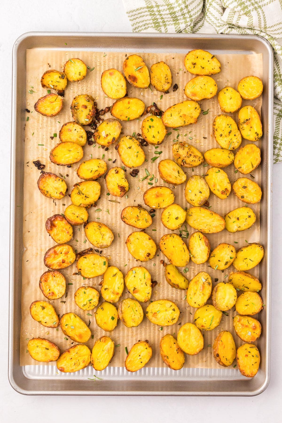 Roasted potatoes with herbs on a baking tray lined with parchment paper.