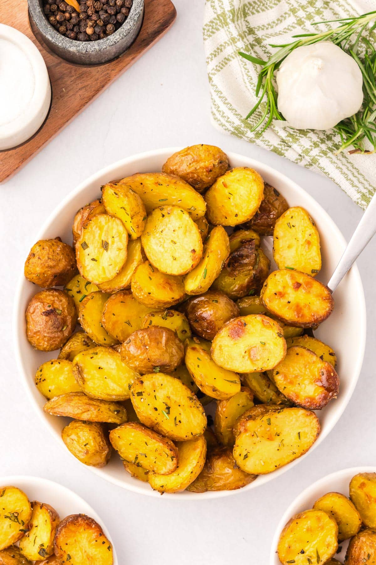 A serving bowl of seasoned, roasted baby potatoes with a serving spoon on a counter from overhead.