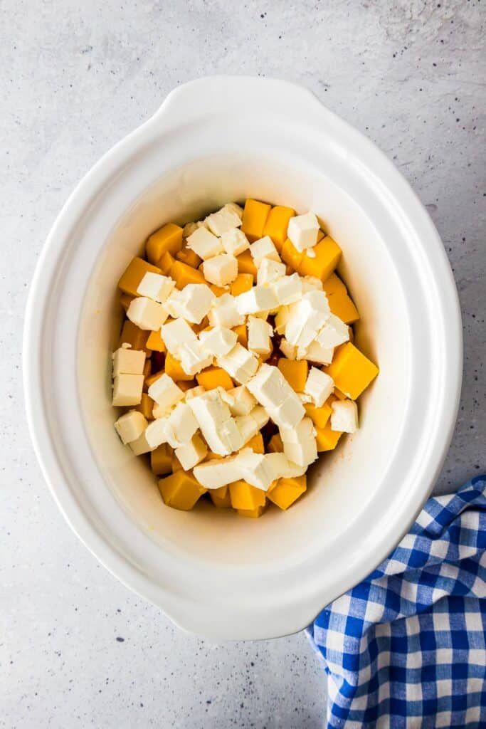 Cubed Velveeta cheese and cream cheese in the base of a slow cooker for crock pot Rotel dip.