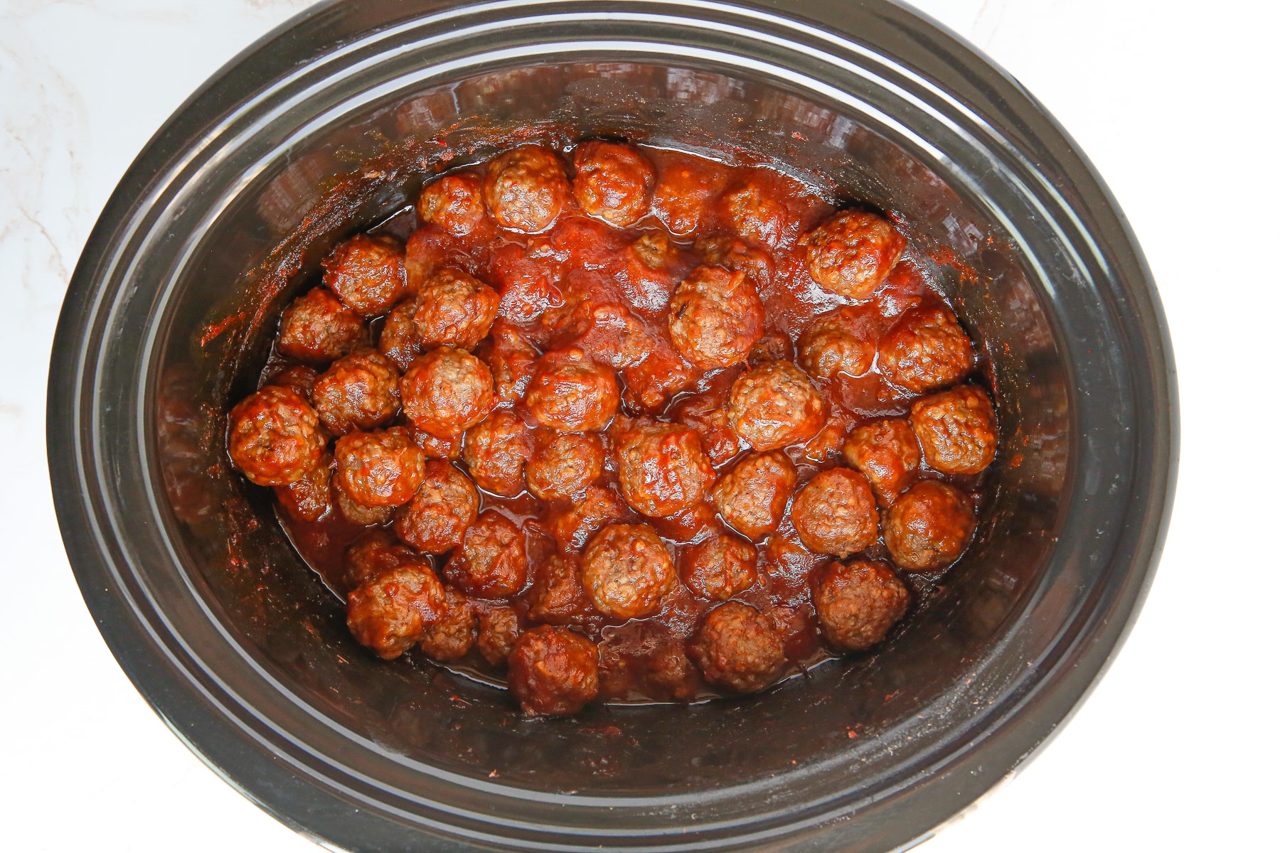 Wide view of a black slow cooker filled with cranberry meatballs.