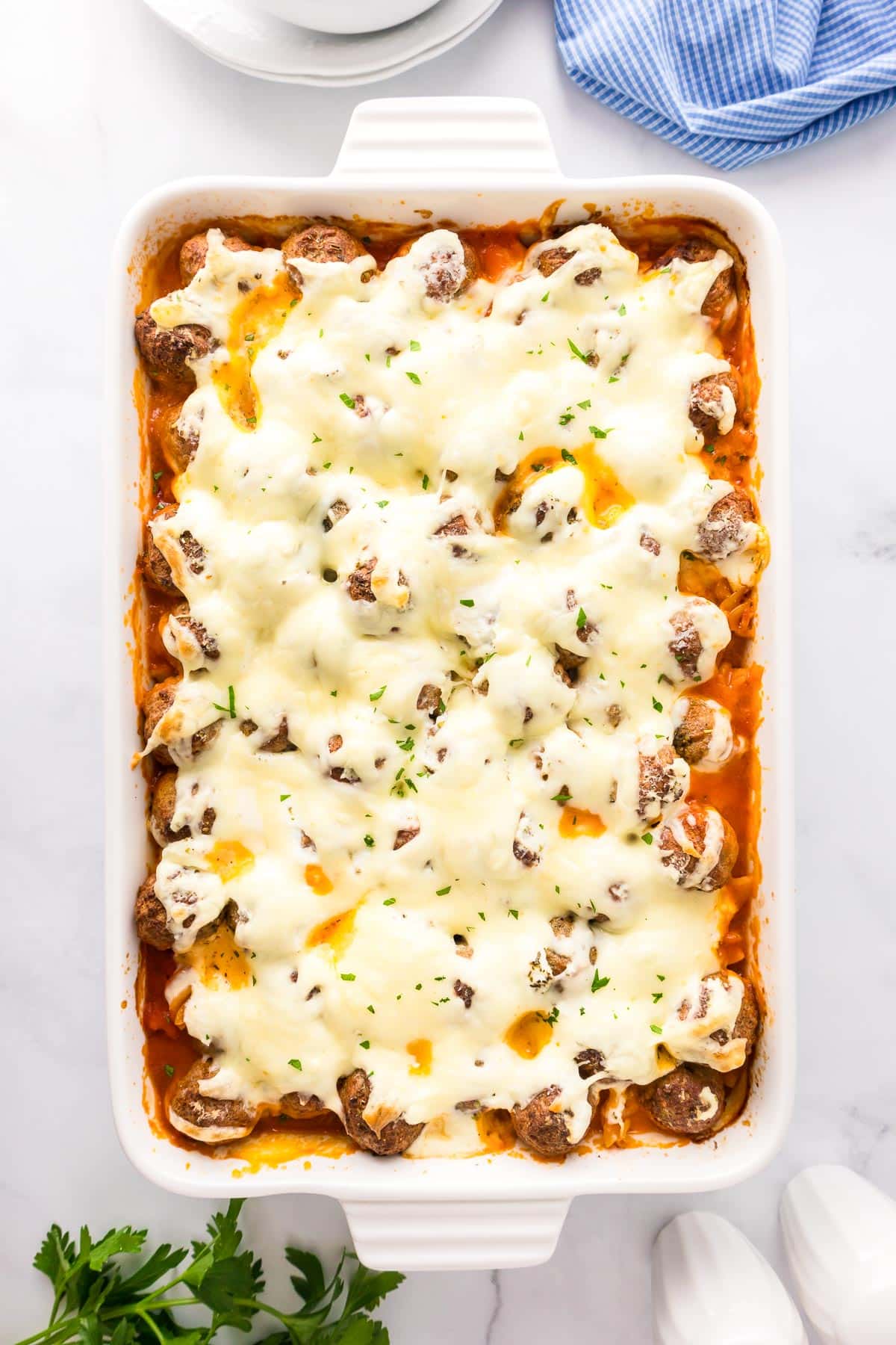 Baked dish with meatballs, melted cheese, and sprinkled herbs in a rectangular white casserole dish on a marble surface.