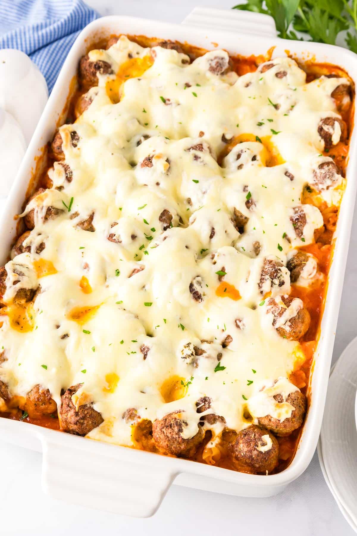 A dump and bake meatball casserole in a baking dish filled with melted mozzarella and ricotta cheese over meatballs and sauce on a counter.