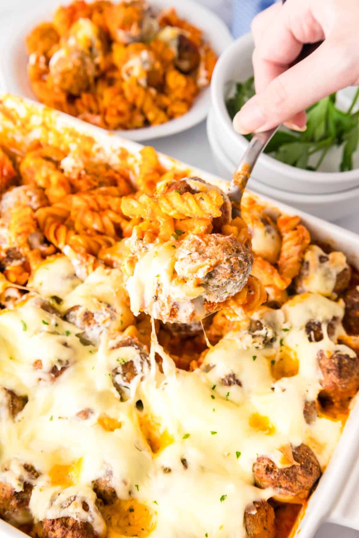 A dump and bake meatball casserole in a pan being served with a spoon with a plateful in the background.