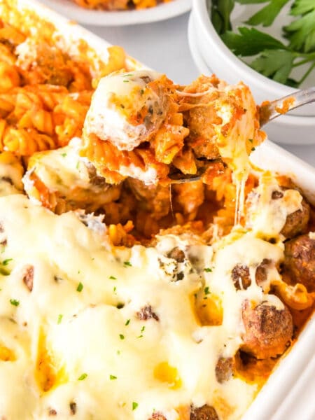 Square view of dump and bake meatball casserole with pasta, meatballs and melted cheese in a baking dish being served with a spoon.