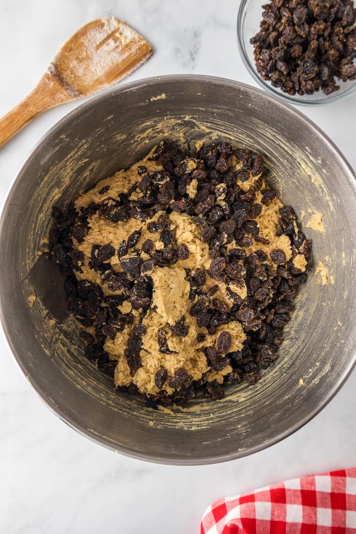 A mixing bowl with raisins being mixed into oatmeal raisin cookie dough.