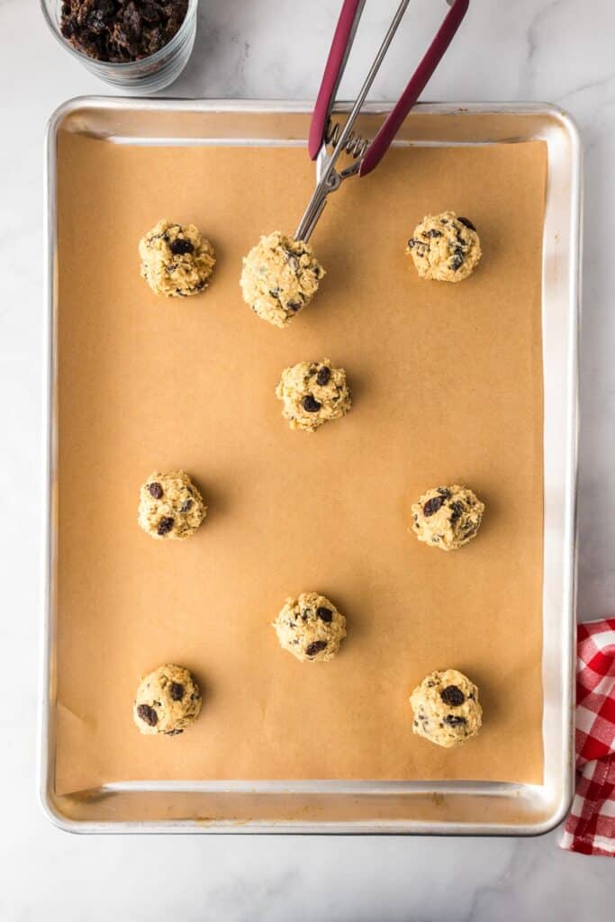 Oatmeal raisin cookie dough balls placed on a baking sheet lined with parchment paper, topped with more raisins.