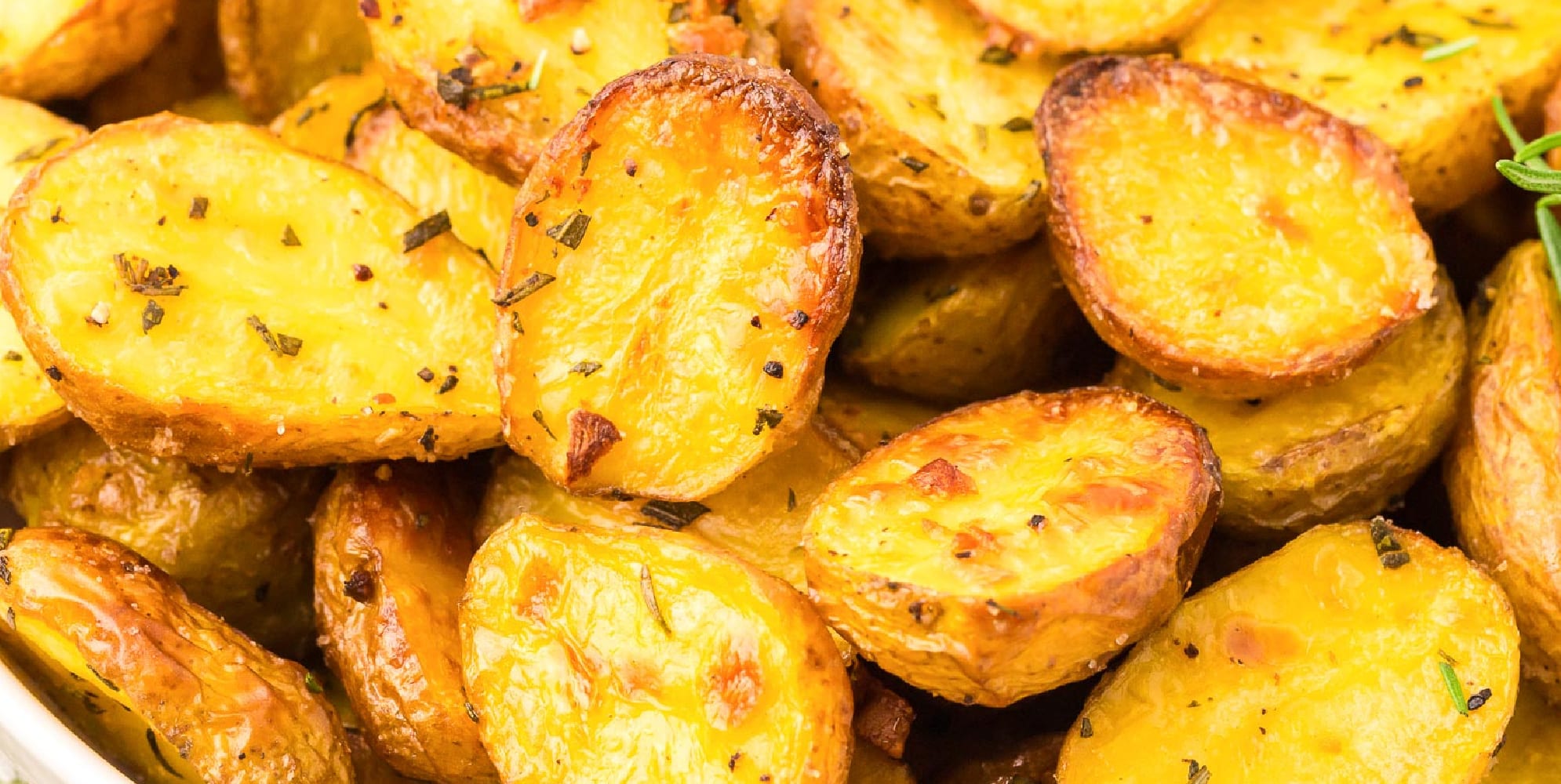 Wide close up view of crispy roasted baby potato halves seasoned with herbs.