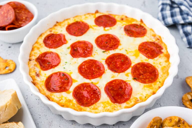 A white baking dish full of pepperoni pizza dip on top of cheese.