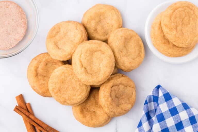 A pile of snickerdoodle cookies on a counter with more cookies and baking supplies nearby.