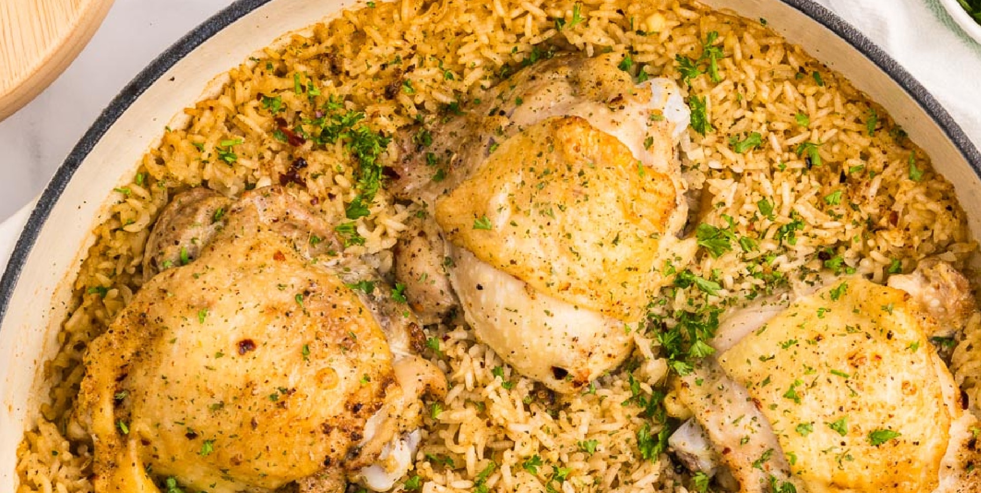 A wide view of bone in chicken thighs on top of rice in a pot from above.