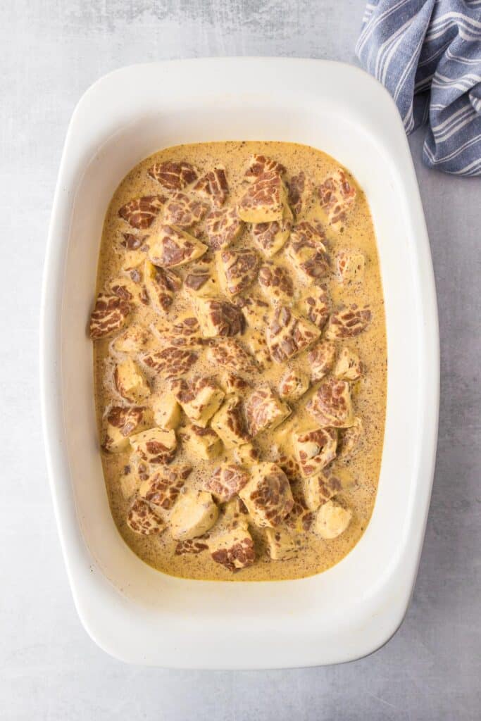 Cinnamon roll dough pieces in a baking sheet covered in an egg milk custard mixture for cinnamon roll casserole.