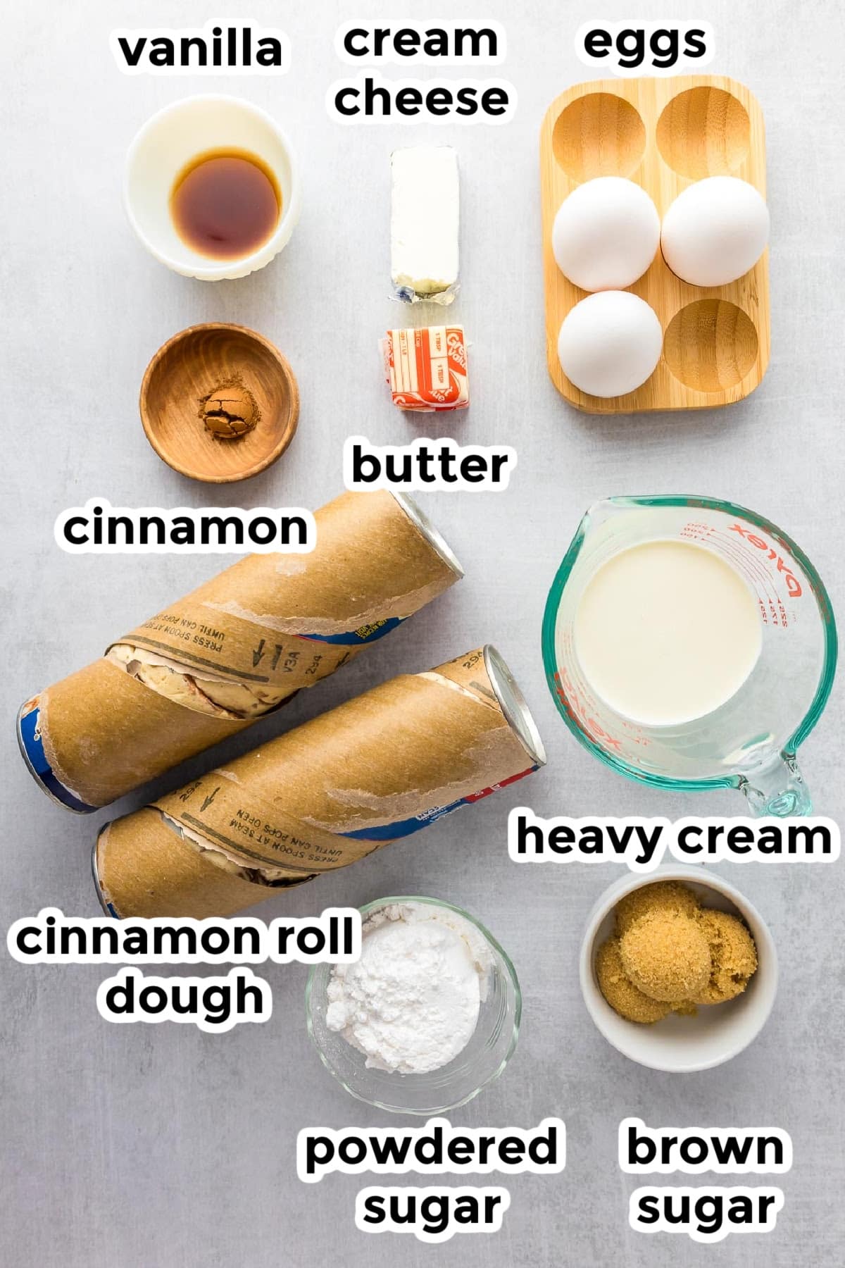 Ingredients for cinnamon roll casserole on a counter in bowls with text labels.