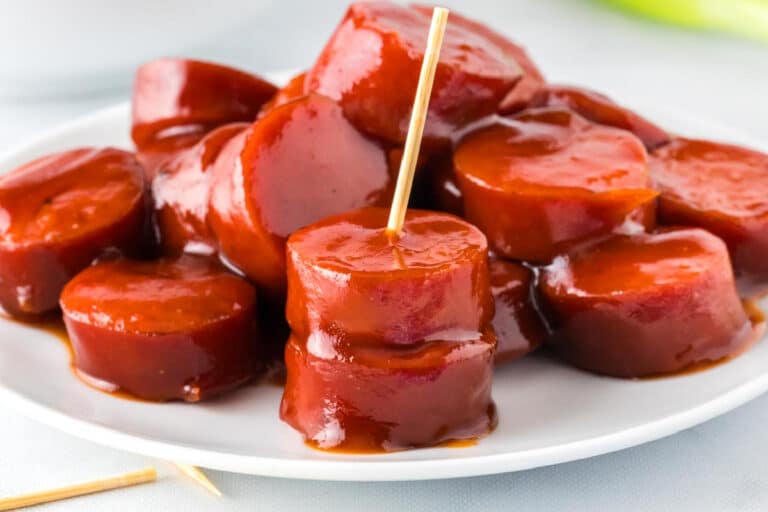 Slices of kielbasa sausage coated in barbecue sauce on a plate, with a toothpick inserted into a piece.