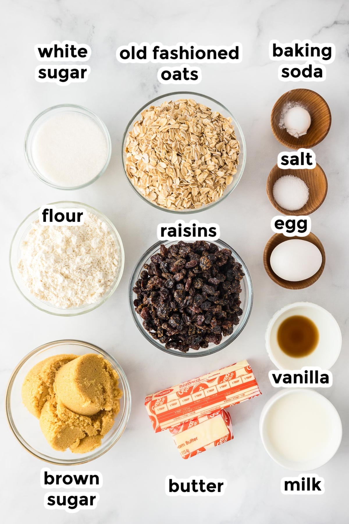 Ingredients for oatmeal raisin cookies on a counter in bowls with text labels.