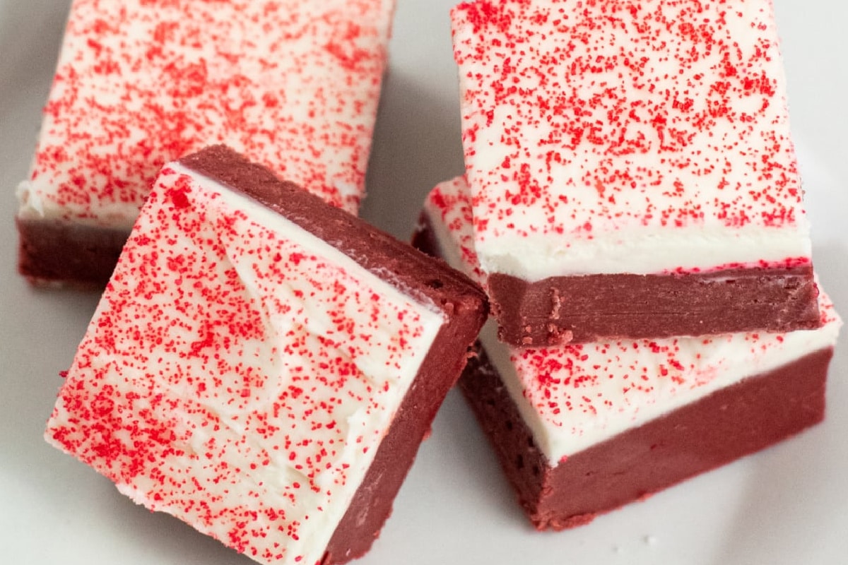 Four red velvet fudge pieces topped with white frosting and red sprinkles on a white plate.