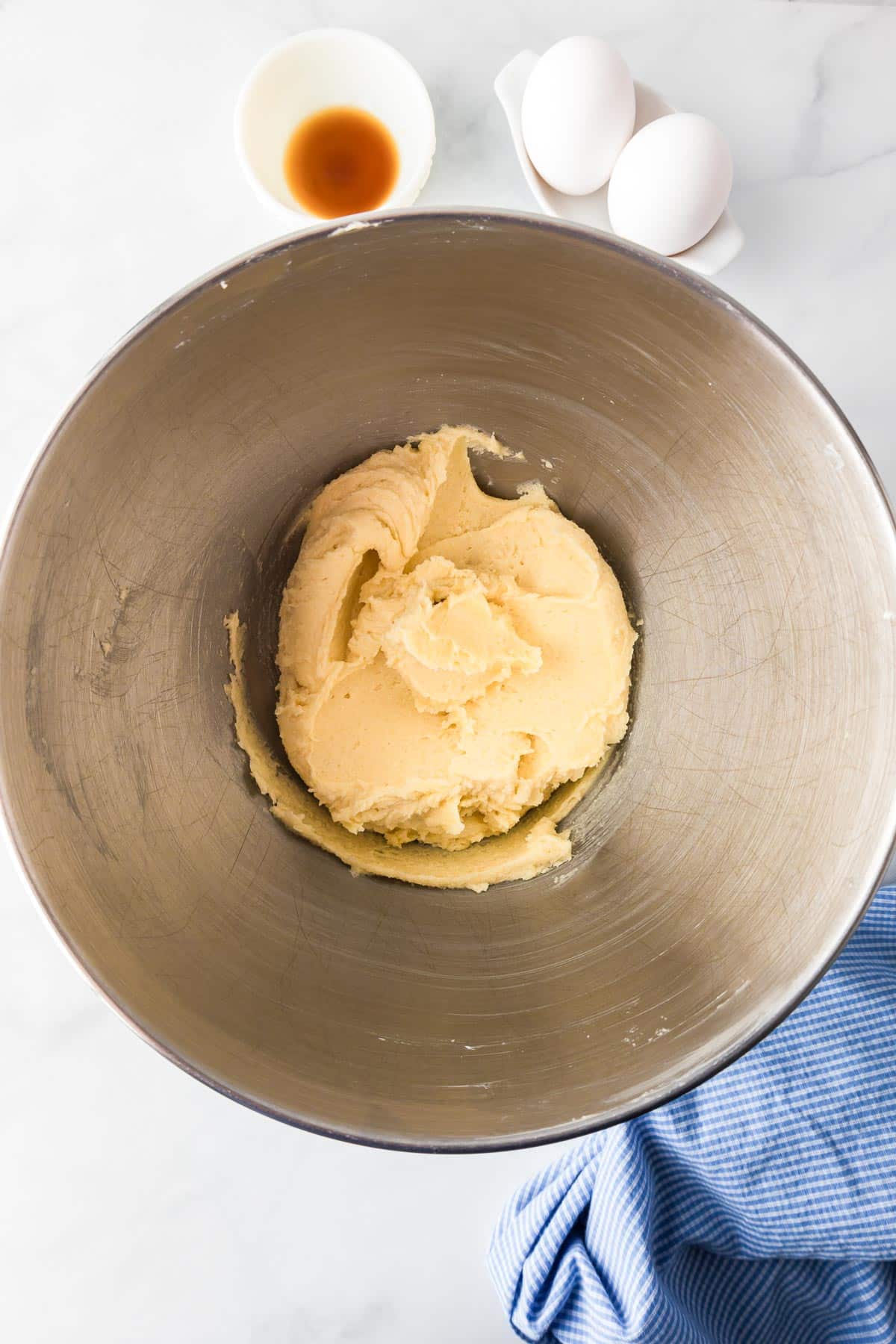 A mixing bowl full of smooth butter creamed with sugar next to a small bowl of vanilla and two eggs on a counter for snickerdoodle cookie bars.