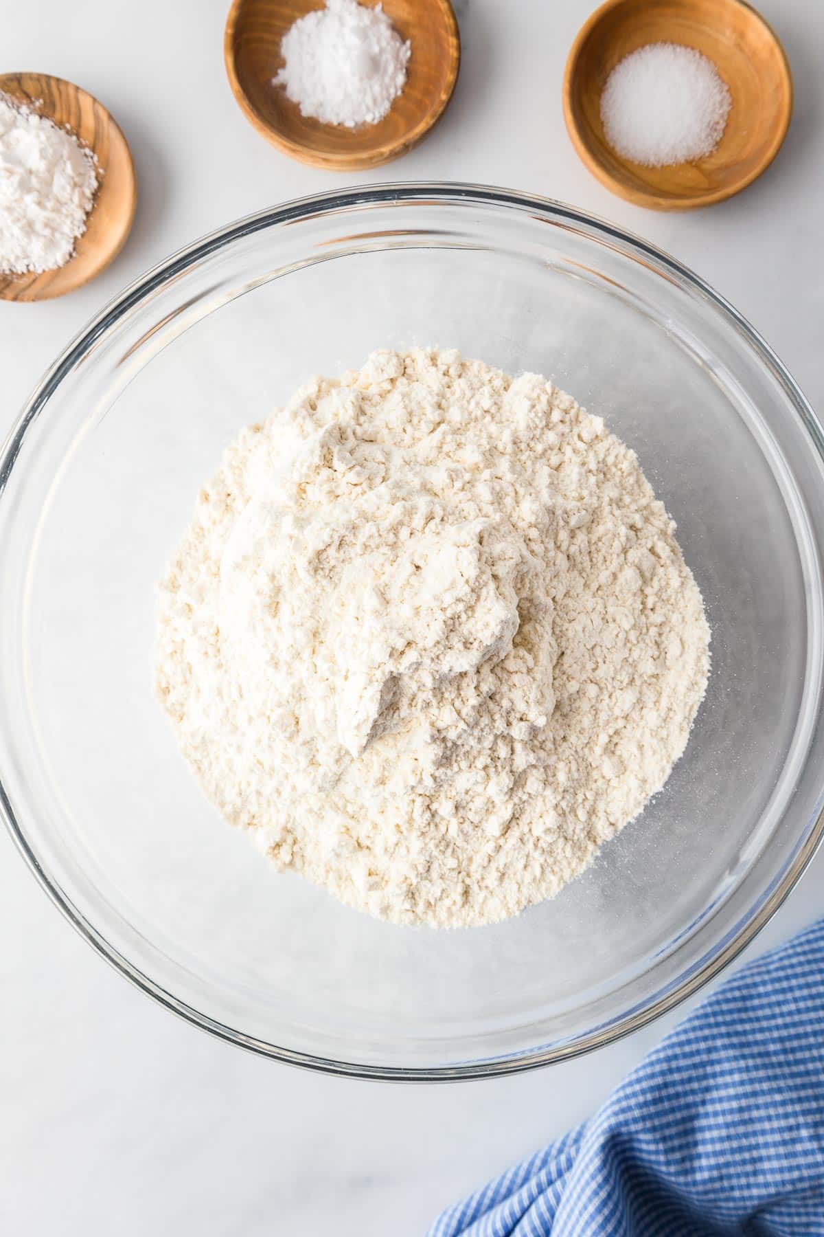 A glass bowl filled with flour next to smaller bowls with baking soda, salt and cream of tartar on a counter for snickerdoodle cookie bars.