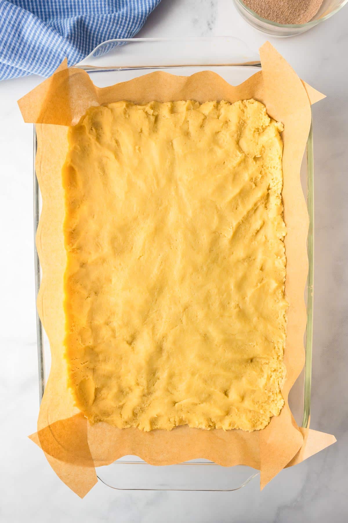 Parchment-lined baking dish filled with Snickerdoodle cookie dough on a counter.