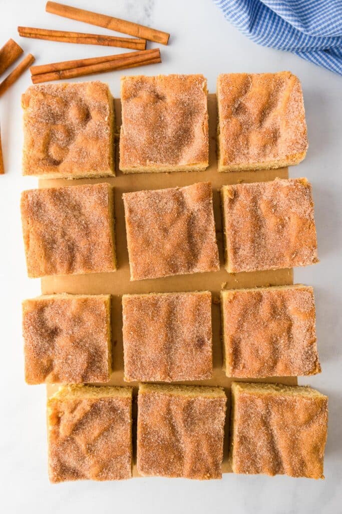 Twelve pieces of snickerdoodle cookie bars sliced on a cutting board on a counter.