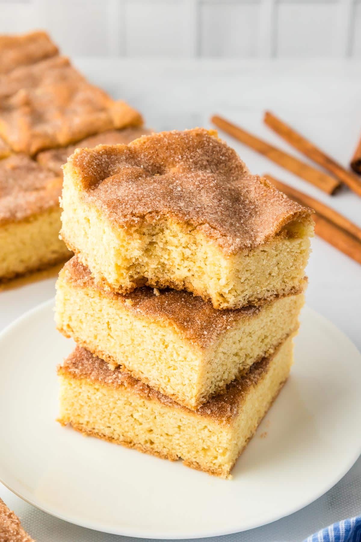 A stack of three cinnamon sugar topped snickerdoodle cookie bars on a plate with the top bar missing a bite.