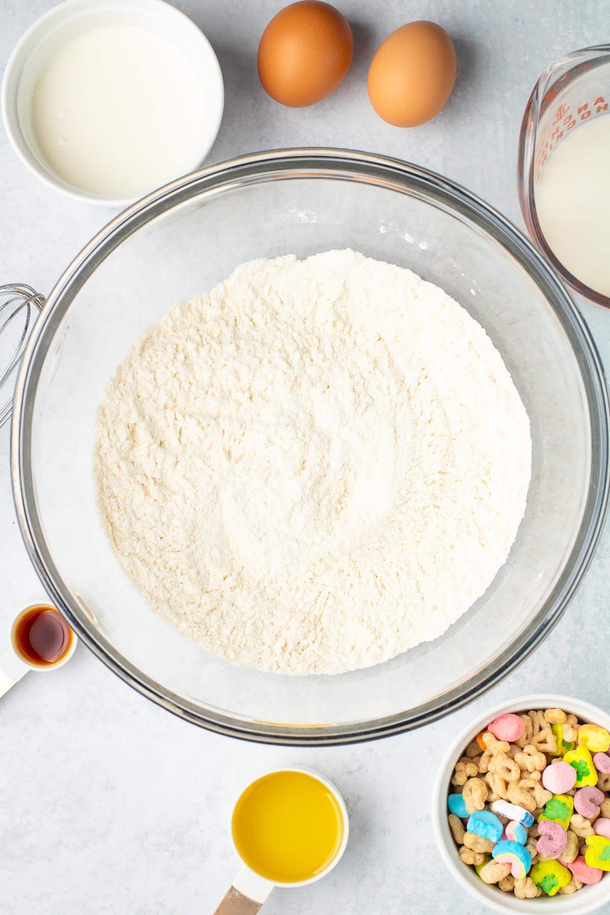 Dry ingredients being mixed together in a mixing bowl for Lucky Charms pancakes with wet ingredients nearby on the counter.