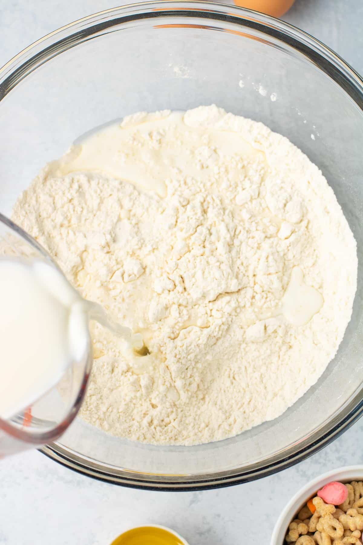 Milk being poured into a glass bowl containing the dry pancake ingredients for Lucky Charm pancakes.