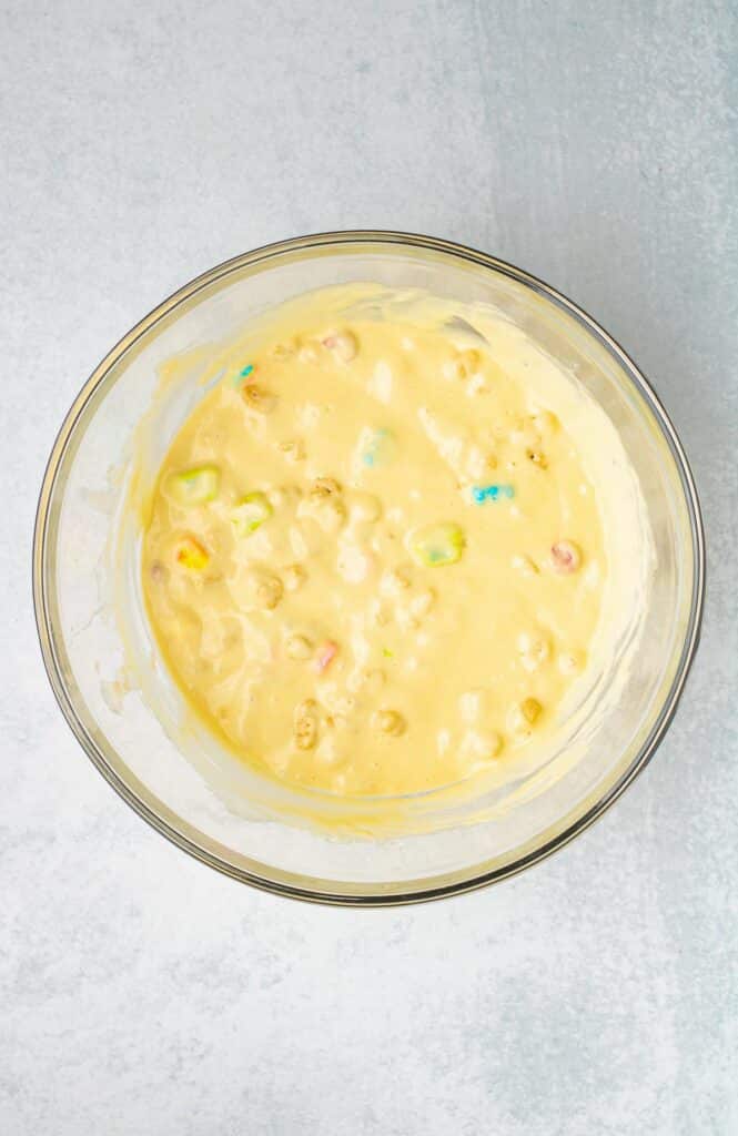 A glass bowl containing a yellow Lucky Charms pancake batter full of colorful cereal pieces on a counter.