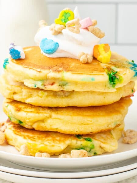 A square view of a stack of Lucky Charm pancakes topped with whipped cream on a plate.