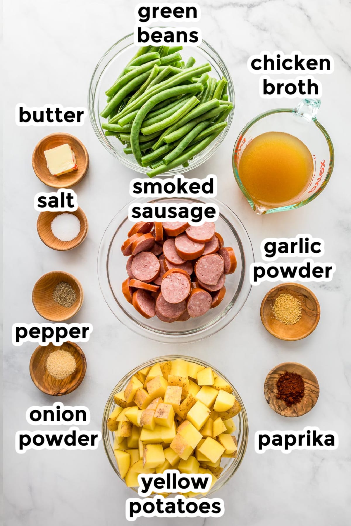 Ingredients for smoked sausage, green beans and potatoes in bowls on a counter with text labels.