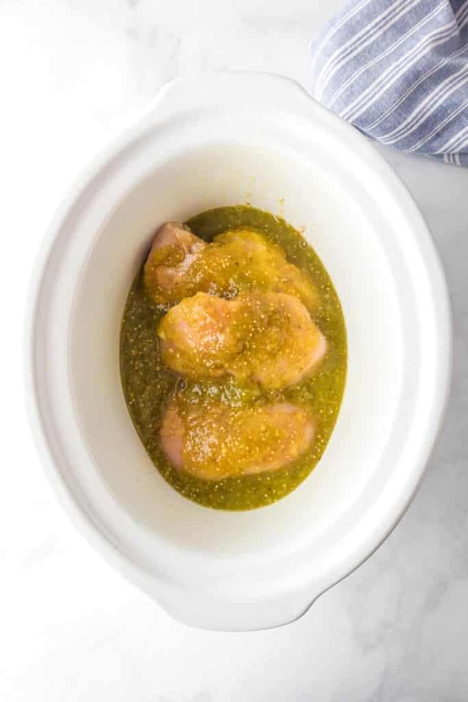 Raw chicken breasts covered in green salsa in a slow cooker base for salsa verde chicken.