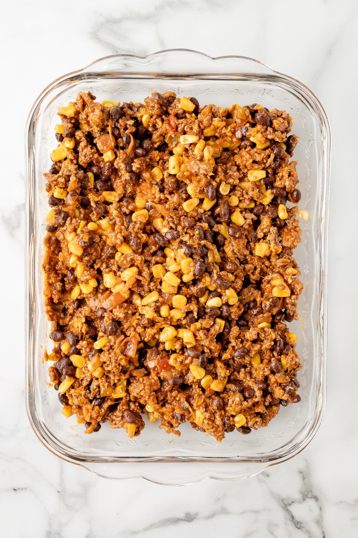 A glass baking dish filled with taco casserole meat, corn and bean filling.