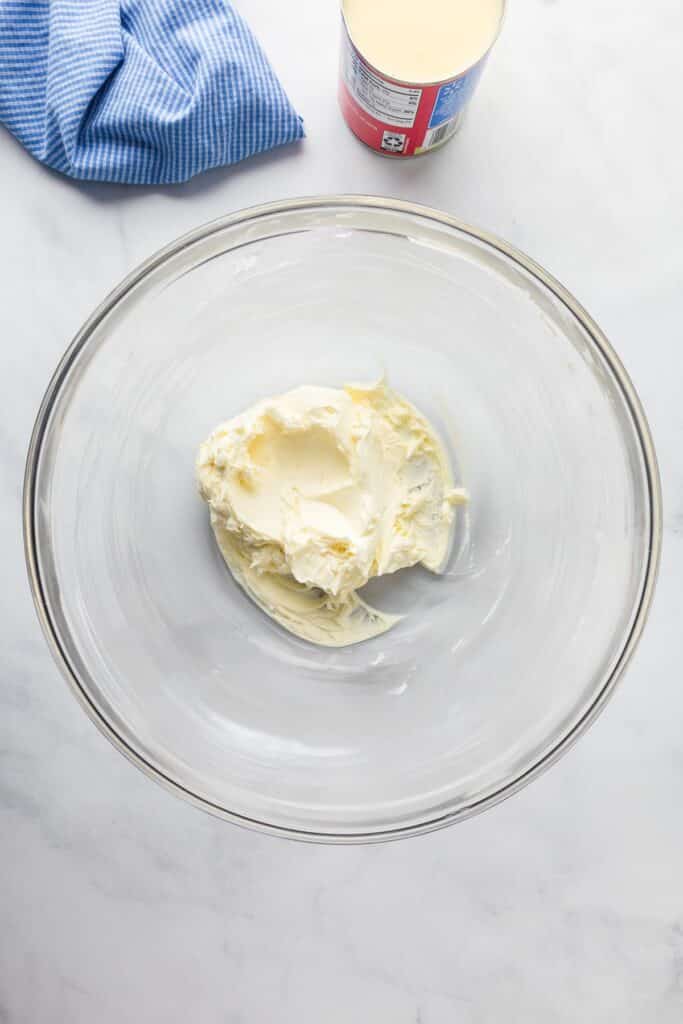 A bowl with softened cream cheese in a bowl next to a can of sweetened condensed milk.