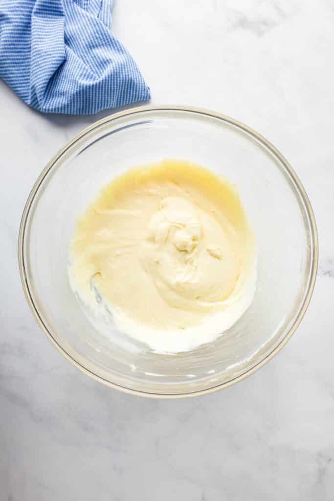 A glass bowl filled with a creamy cream cheese and condensed milk mixture after blending.